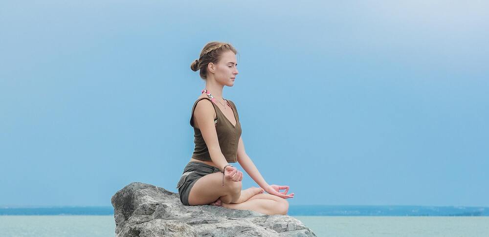 Person sitzt meditierend auf einem Stein